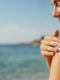 Una donna al rientro dalle vacanze che applica una crema idratante e nutriente sulle spalle e sul viso vicina a una finestra.